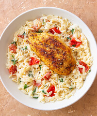 Orzo pasta with fried chicken breast, tomatoes and herbs. Italian food.