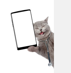 Happy cat wearing like a doctor with stethoscope on his neck showing big smartphone with blank screen in it paw from behind blank white banner. Empty space for text. isolated on white background