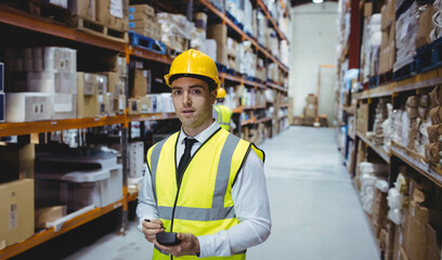 Male warehouse worker wearing hardhat reflective vest in aisle scanning boxes on racks with scanner