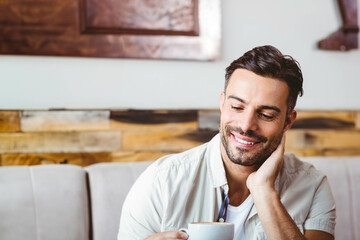 Male wearing button-up shirt sitting on bench in cafe holding ceramic mug resting cheek, copy space