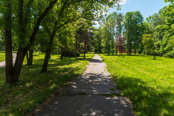 Public park with trees, meadow and footpath during partly cloudy springtime day