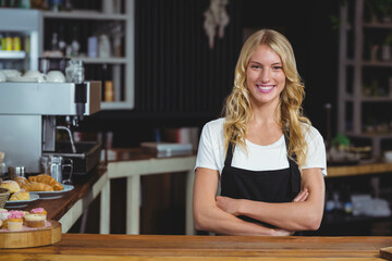 Smiling female barista wearing apron behind counter at cafe with espresso machine, copy space
