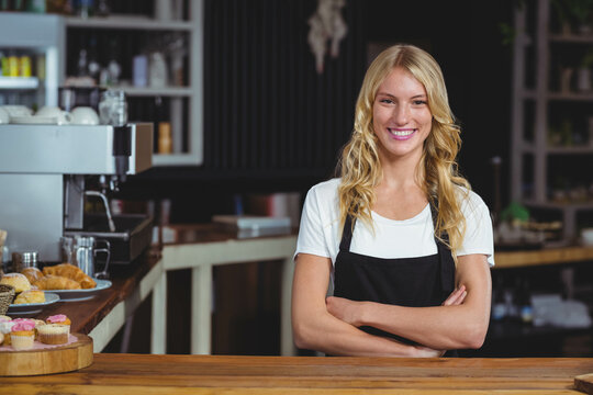 Smiling female barista wearing apron behind counter at cafe with espresso machine, copy space - Powered by Adobe