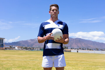 Male athlete wearing striped jersey and white shorts standing on sports field holding rugby ball