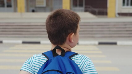 Boy with backpack waiting at crosswalk near the street, Child standing by zebra crossing as car approaches the road, Kid with blue backpack prepares to cross the busy street, Schoolchild on crosswalk - Powered by Adobe