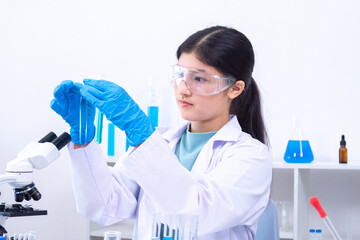 A teenage girl scientist in a laboratory carefully inspects liquid sample in pipette while wearing...