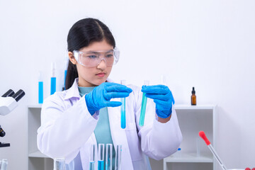A teenage girl scientist in a laboratory carefully inspects liquid sample in pipette while wearing...