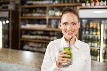 Female bartender standing behind bar counter serving cocktail with lime slices mint ice black straw