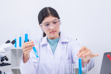 Teen girl scientist in labcoat and safety glasses performing chemistry experiment with pipette and...