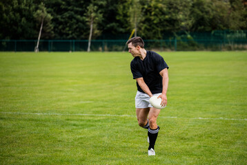 Male athlete standing on grassy field in sportswear holding white rugby ball by fence, copy space