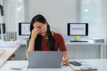 Stressed asian businesswoman suffering from headache while working on laptop in office