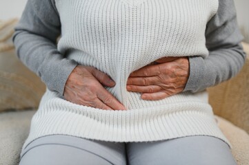 Mature woman suffering from stomach ache sitting on a bed in the bedroom. Senior woman sitting on...