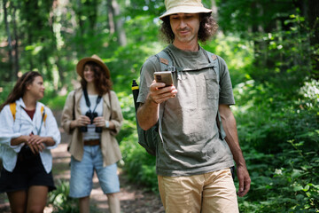 Group of happy young people friends hiking with camera binoculars and backpacks , walking in summer forest