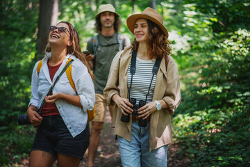 Group of happy young people friends hiking with camera binoculars and backpacks , walking in summer forest