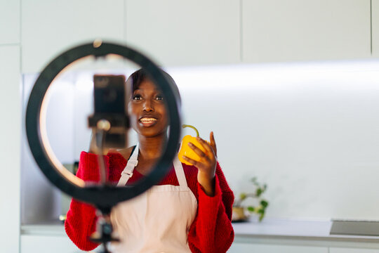 Food blogger recording a video showing a yellow pepper in a modern kitchen