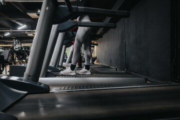 A focused perspective of a person jogging on a treadmill inside a modern gym with other equipment in the background, emphasizing exercise, health, and fitness.