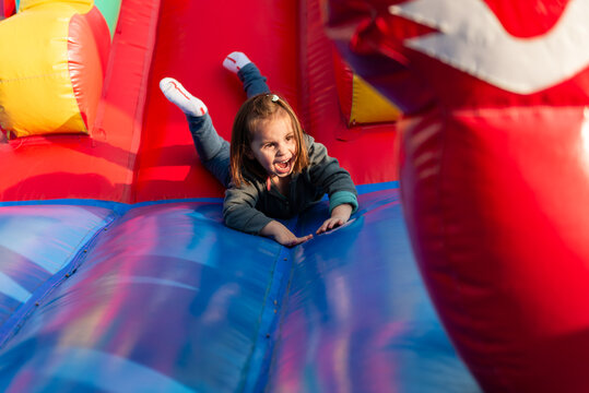 Excited girl sliding down inflatable bouncy house at playground