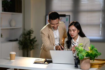 Business colleagues working together at laptop, discussing ideas and reviewing project data in an office