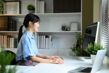 Smiling Asian woman working at desktop computer in a bright, modern office space