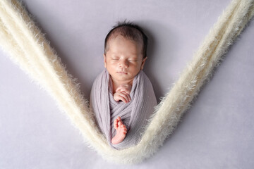 This newborn photo features a half-month-old Japanese baby, sleeping in a soft swaddle. The baby...