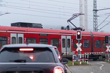 Wartende Autos am geschlossenen Bahnübergang mit durchfahrendem Zug 