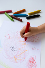 Child hand drawing with colorful crayons on white paper