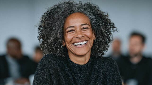 Smiling woman with gray hair in a meeting or conference setting.