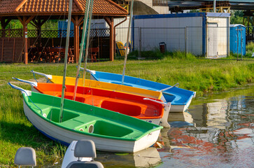 Several rowing boats moored by the shore of a small body of water, near a wooden shelter and...