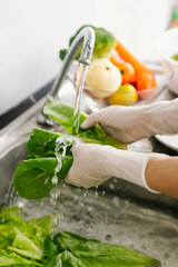 Woman washing fresh vegetables at kitchen sink, practicing hygiene and food safety indoors to prevent illness during pandemic, ensuring healthy lifestyle and cleanliness.