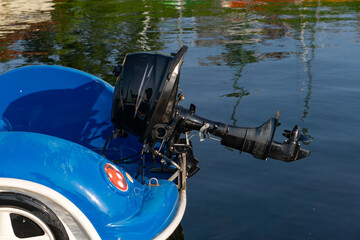 Obraz premium outboard motor mounted on a blue car-shaped boat moored on calm water in a marina.
