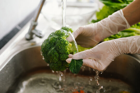 Woman washing fresh vegetables at kitchen sink, practicing hygiene and food safety indoors to prevent illness during pandemic, ensuring healthy lifestyle and cleanliness. - Powered by Adobe