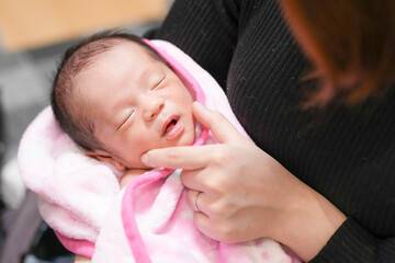 A half-month-old Japanese newborn is wrapped in a pink blanket and held in the loving arms of both...