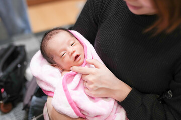 A half-month-old Japanese newborn is wrapped in a pink blanket and held in the loving arms of both...