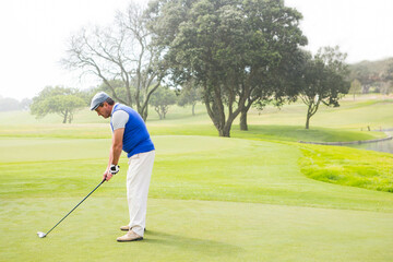 Senior male golfer standing on trimmed fairway near pond wearing golf glove and gripping club