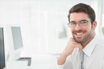 Fototapeta premium Businessman smiling and resting chin on hand at office desk with monitor, keyboard, copy space