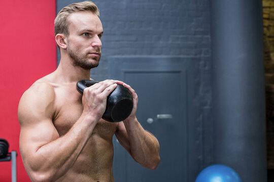 Man lifting black kettlebell in gym weight area showing dumbbell rack and exercise ball, copy space