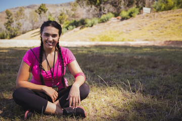 woman in her twenties sitting crosslegged in meadow wearing sweatband holding whistle near sneakers