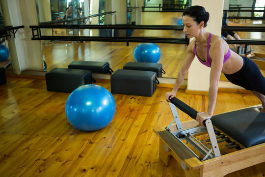 Fototapeta Woman performing Pilates on reformer in studio with wood floors, mirrors, foam blocks, blue ball