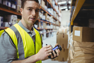 Male warehouse associate scanning boxes in warehouse using barcode scanner and stylus, copy space