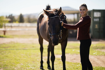 Female rider standing beside dark brown horse holding halter lead rope in paddock with stable