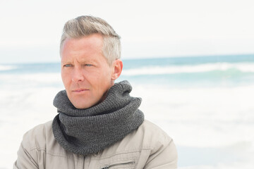 Fototapeta premium Man in early 50s standing on sandy beach wearing beige zip-up jacket and grey knit scarf