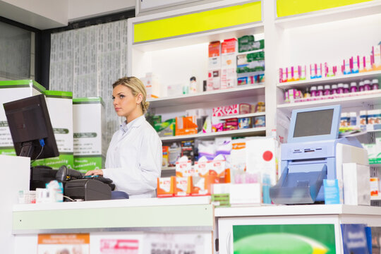 Woman pharmacist typing on keyboard behind pharmacy counter with barcode scanner, copy space