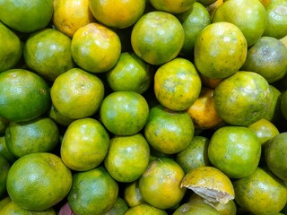 A vibrant pile of fresh, ripe oranges with mottled green and yellow peels. A beautiful, natural texture and color backdrop for healthy food and citrus-related content