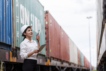 A female transport officer in a hard hat holds a clipboard and walkie-talkie, inspecting cargo...