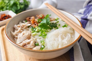 Clear chicken noodle soup with thin rice noodles in ceramic bowl with chopsticks