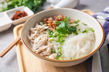 Clear chicken noodle soup with thin rice noodles in ceramic bowl with chopsticks
