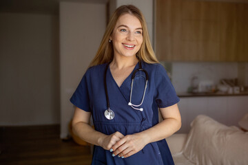 Smiling healthcare worker in navy scrubs standing in a warm, light-filled room
