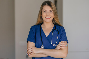 Smiling female nurse in uniform with stethoscope crossing arms in healthcare setting