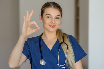 Confident medical professional showing okay hand sign wearing stethoscope and scrubs