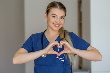 Smiling nurse in blue scrubs showing heart gesture with her hands